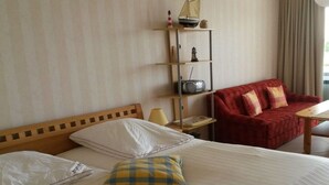 Ett hotellrum med en säng, en röd soffa, ett litet bord och en hylla med dekorativa föremål.