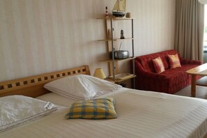A hotel room with a bed, a red sofa, a small table, and a shelf with decorative items. - Holiday apartment with 1 bedroom (Fehmarn)