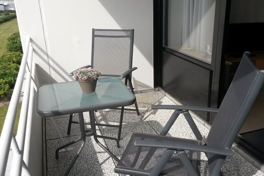 Un balcón con una mesa de vidrio y dos sillas, una planta en maceta y vistas al verdor.