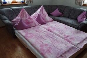 Ein Zimmer mit einem grauen Sofa, einem Bett mit rosa floralem Bettzeug und violetten Kissen.