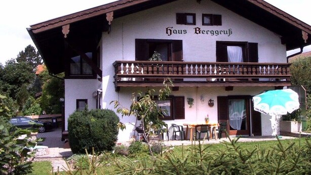 Um edifício de dois andares com uma varanda e uma placa com a inscrição 'Haus Berggüß'.
