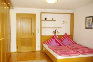 A bedroom with a wooden door, a bed with pink and purple bedding, and a shelf with decorative items. - Haus Berggruß EG with Chiemgau map (Ruhpolding)