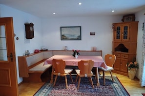 Un comedor con una mesa preparada para cuatro personas, sillas de madera, un banco, un reloj y un armario.