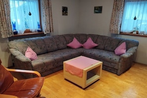 Una sala de estar con un sofá modular, una mesita de madera y un sillón de cuero marrón.