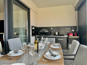 Un coin repas avec une table dressée pour six personnes, une cuisine équipée d’appareils modernes et une grande fenêtre laissant entrer la lumière naturelle.