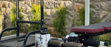 An outdoor gym setup with exercise equipment, a stone wall, and a metal fence.