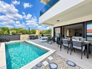 Ein moderner Poolbereich im Freien mit Essplatz und Blick auf die umliegende Landschaft.