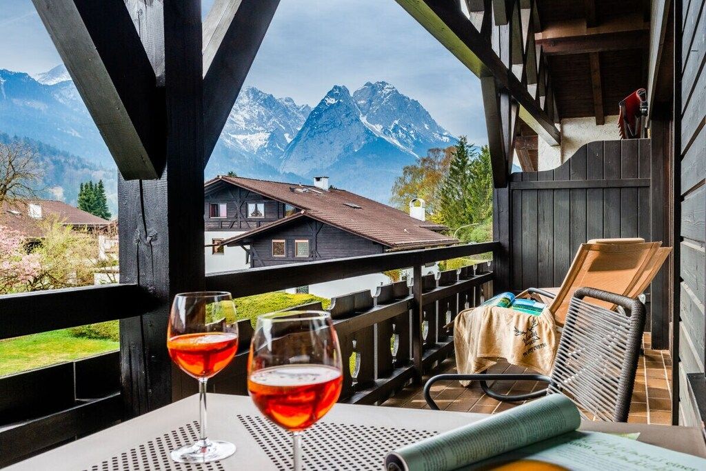 A balcony with a mountain view, two glasses of red wine, and a chair.