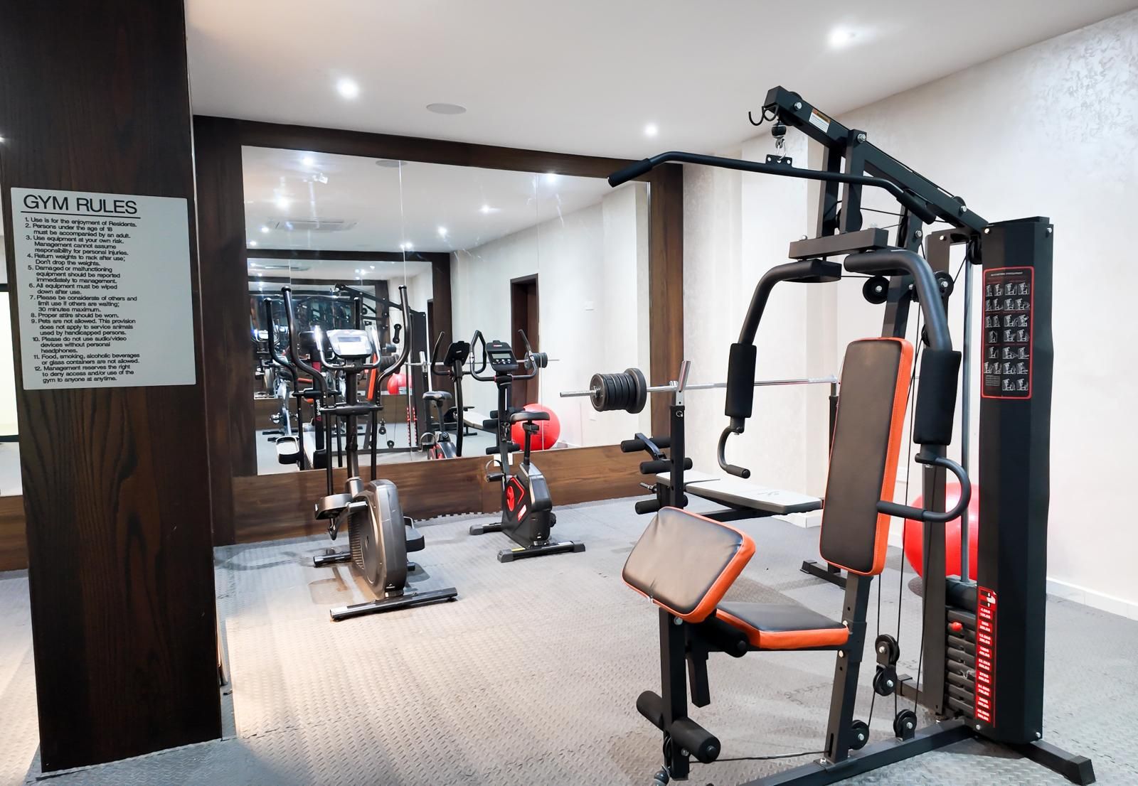 A gym with exercise equipment, a mirror, and a sign listing gym rules.
