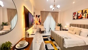 Quarto de hotel moderno com uma cama grande, área de estar com cadeiras, mesa de jantar e um espelho amplo.