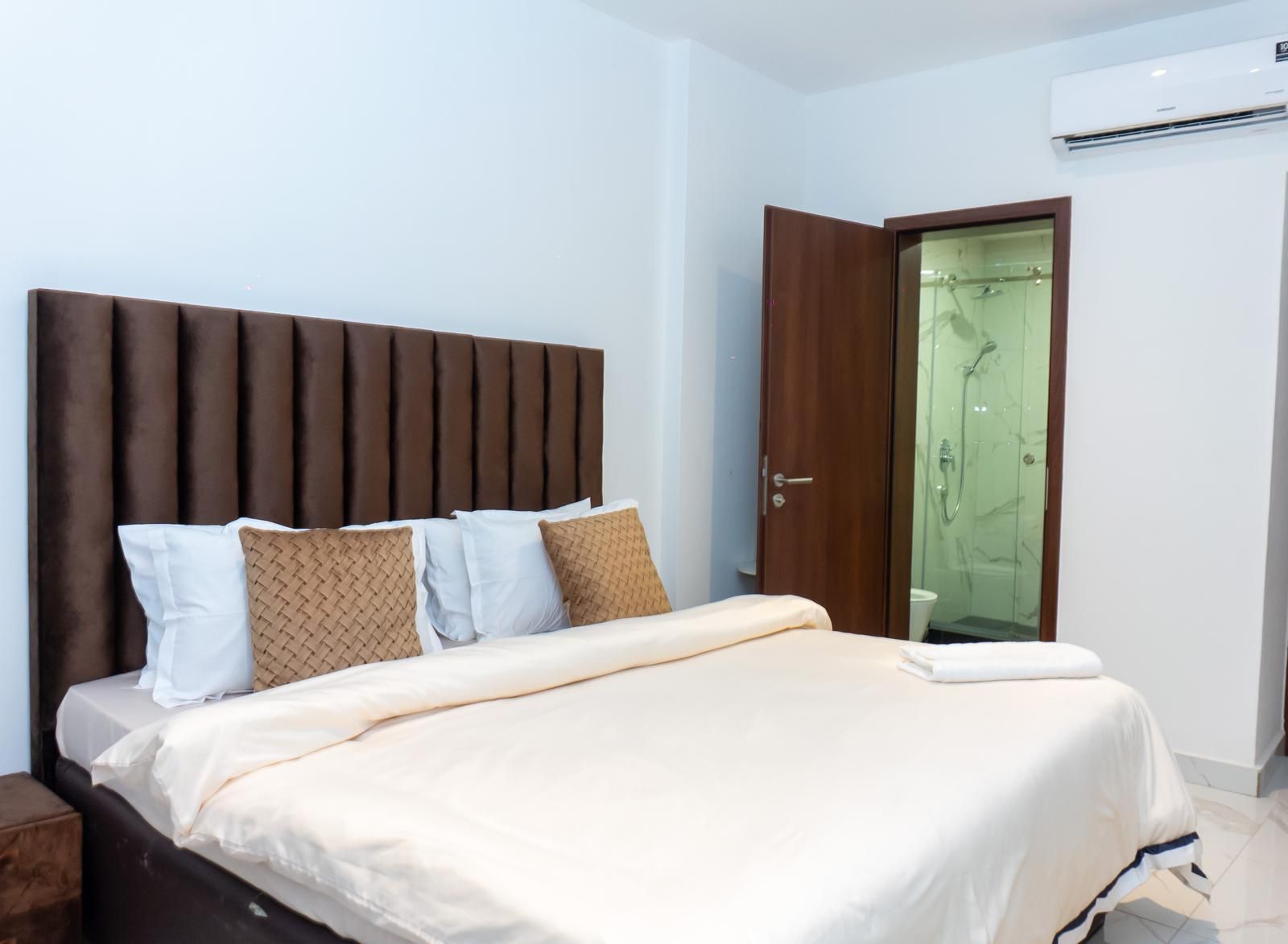 Un dormitorio con cama, almohadas, cabecero de madera, una puerta y un equipo de aire acondicionado.