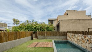 Ein Garten mit Pool, einer Holzterrasse und einer Steinmauer.
