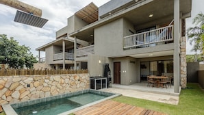Ein modernes, mehrgeschossiges Haus mit Swimmingpool, Essbereich im Freien und einer Steinmauer.