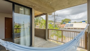 Un balcón con una hamaca, una puerta de cristal y vistas a edificios y árboles.