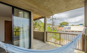 Un balcón con una hamaca, una puerta de cristal y vistas a edificios y árboles.