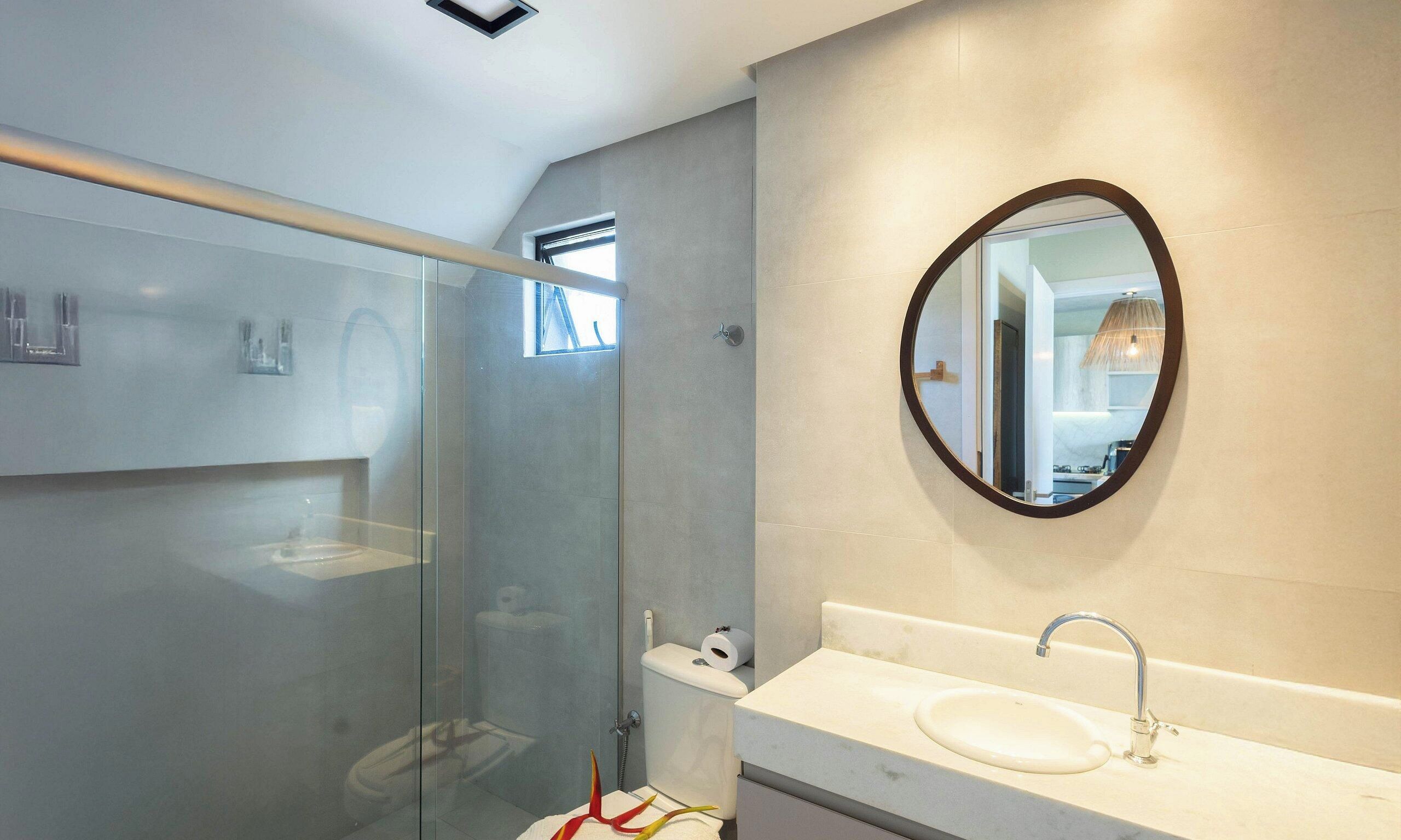 A modern bathroom with a glass-enclosed shower, a round mirror, and a white sink.