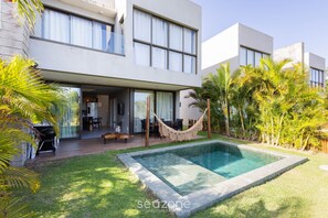 Ein modernes, zweistöckiges Haus mit Pool, Sitzgelegenheiten im Freien und üppiger Bepflanzung.
