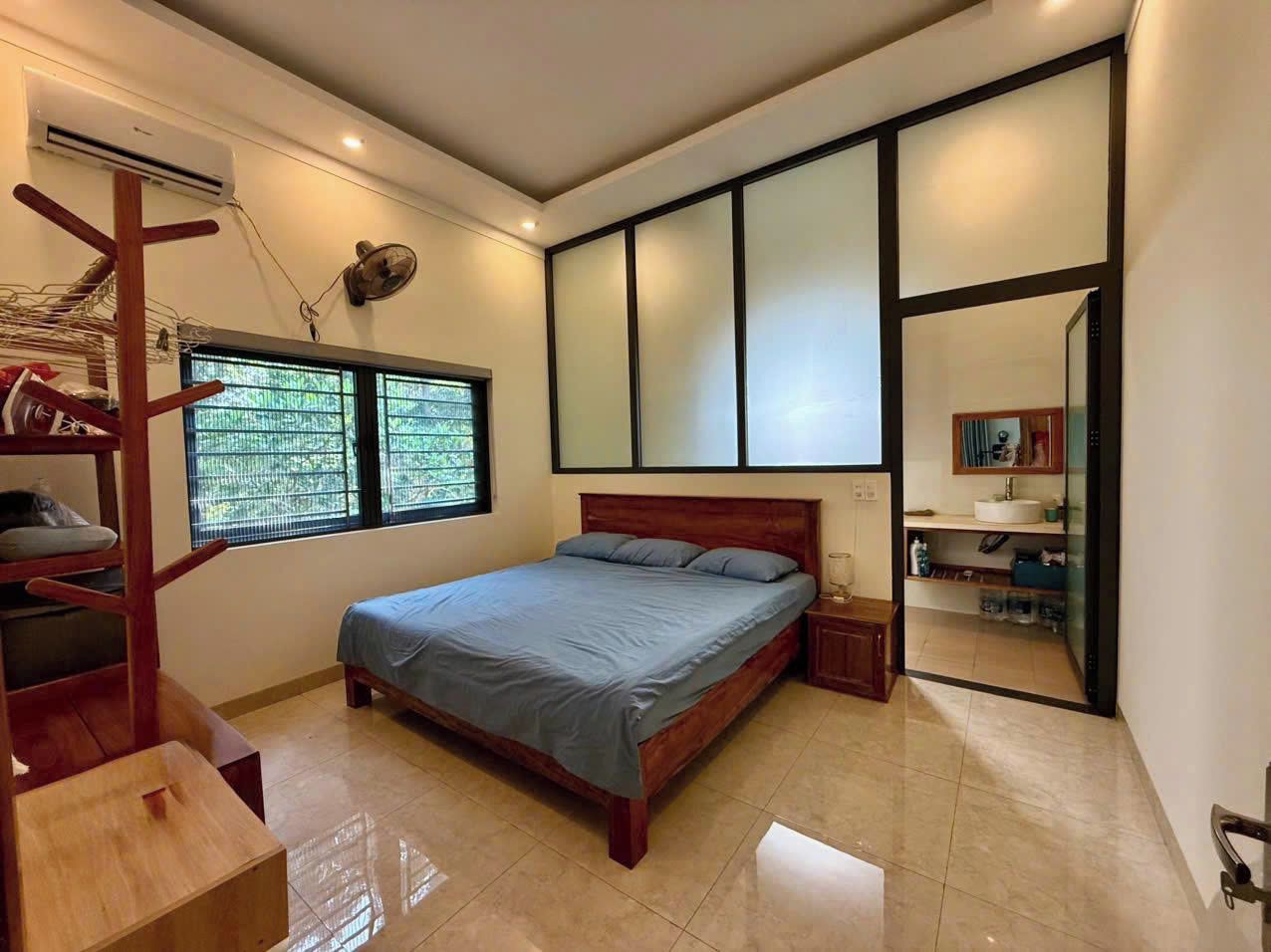 A bedroom with a bed, a window, a fan, a shelf, and a mirror.