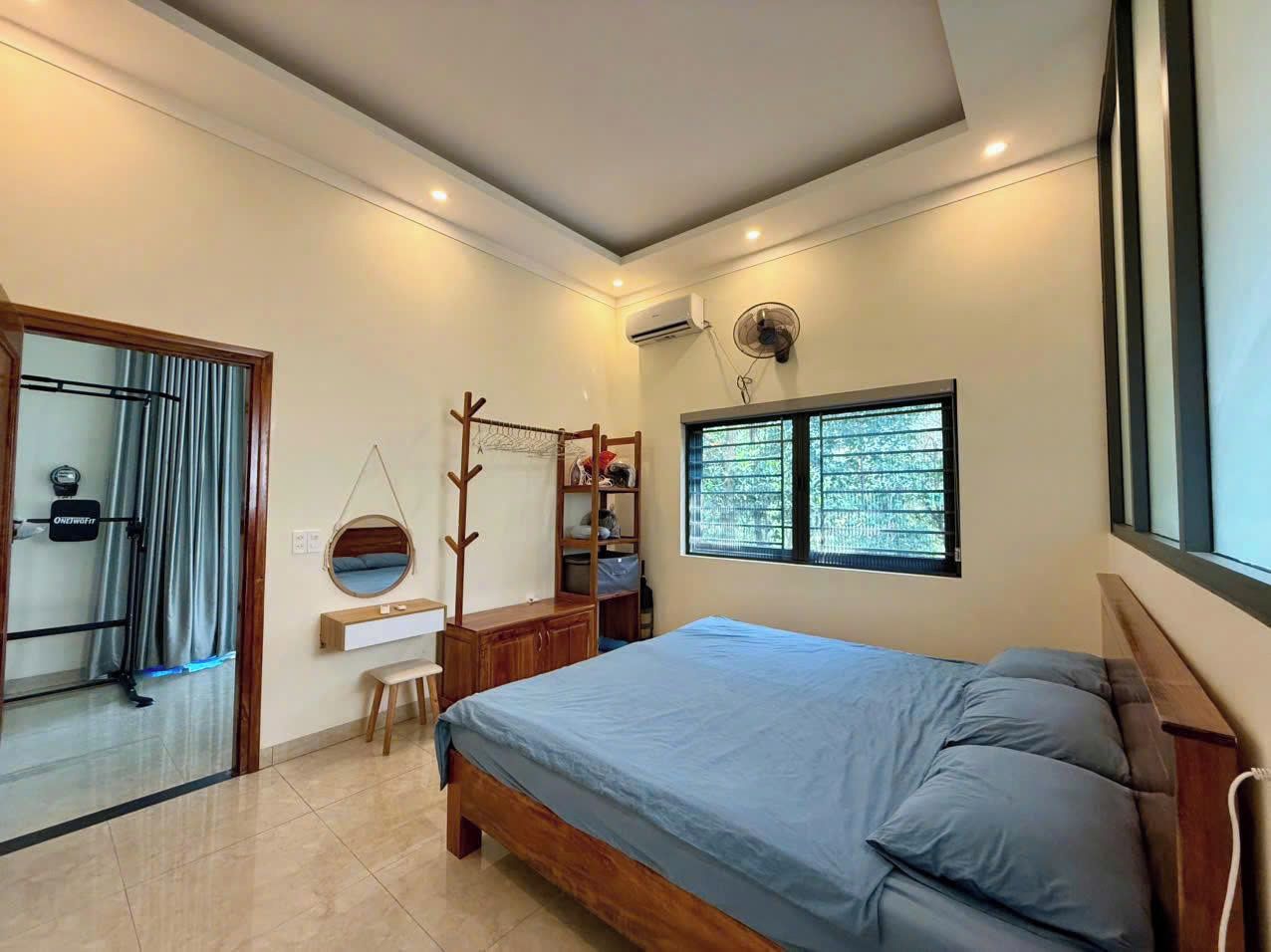 A bedroom with a bed, a desk, a chair, a hanging coat rack, and a window with blinds.