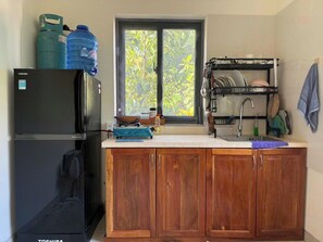 A compact kitchen with a refrigerator, a dish rack, and a window with a view of greenery. - Cozy 2BR Garden Villa #2 - Eco Cay Sao Phu Quoc (Thành phố Phú Quốc)