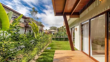 Uma casa moderna com um deck de madeira, um gramado verde e uma grande porta de vidro.