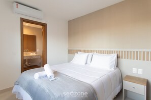 Quarto de hotel com cama, mesa de cabeceira, banheiro com espelho e unidade de ar condicionado.