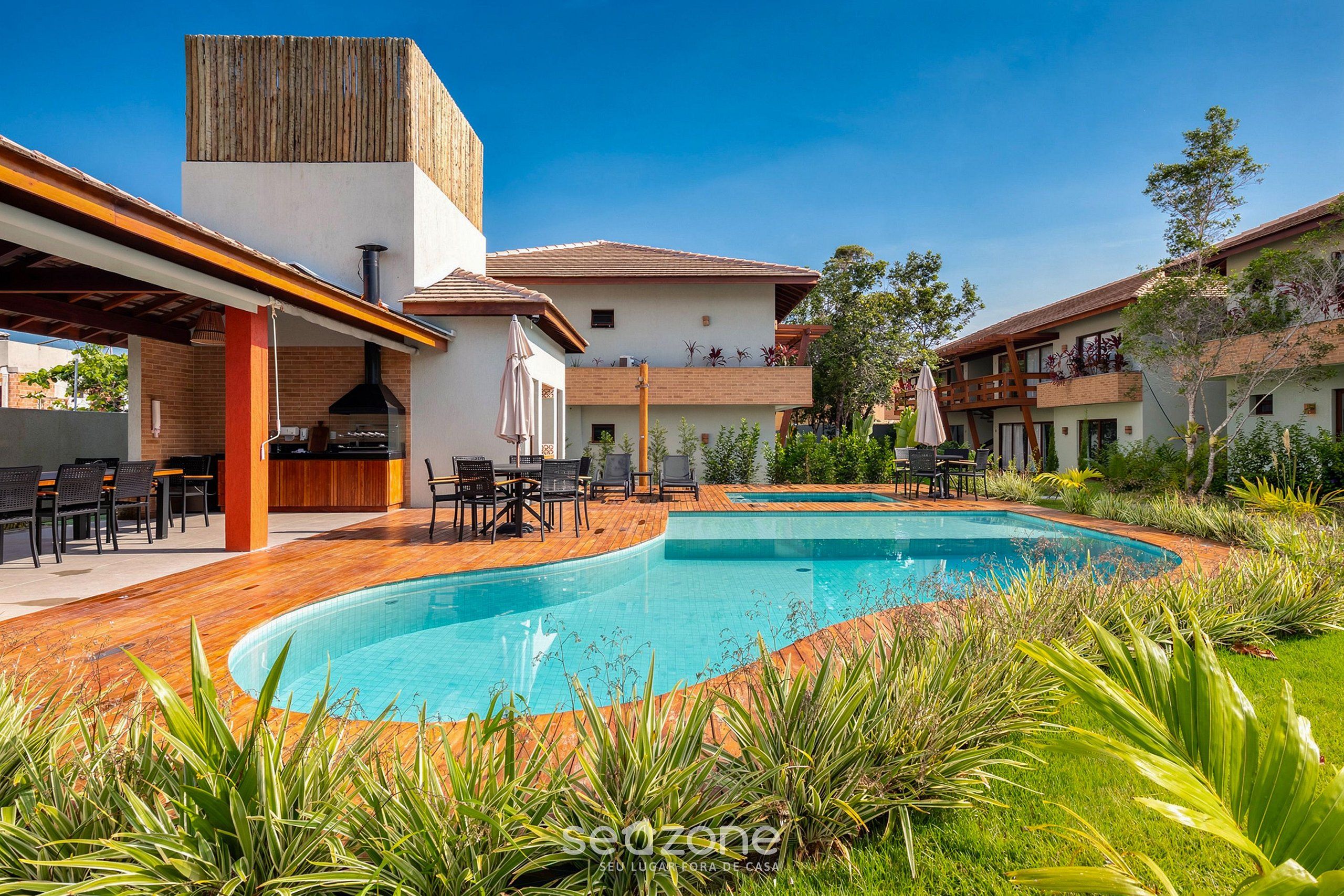 Ein Poolbereich mit Holzterrasse, Sitzgelegenheiten im Freien und Grillplatz.