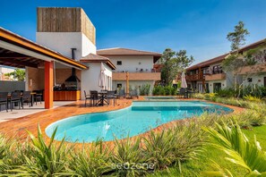 A pool area with a wooden deck, outdoor seating, and a barbecue area. - House in Arraial D'ajuda With Pool Pcr0006 (Porto Seguro)