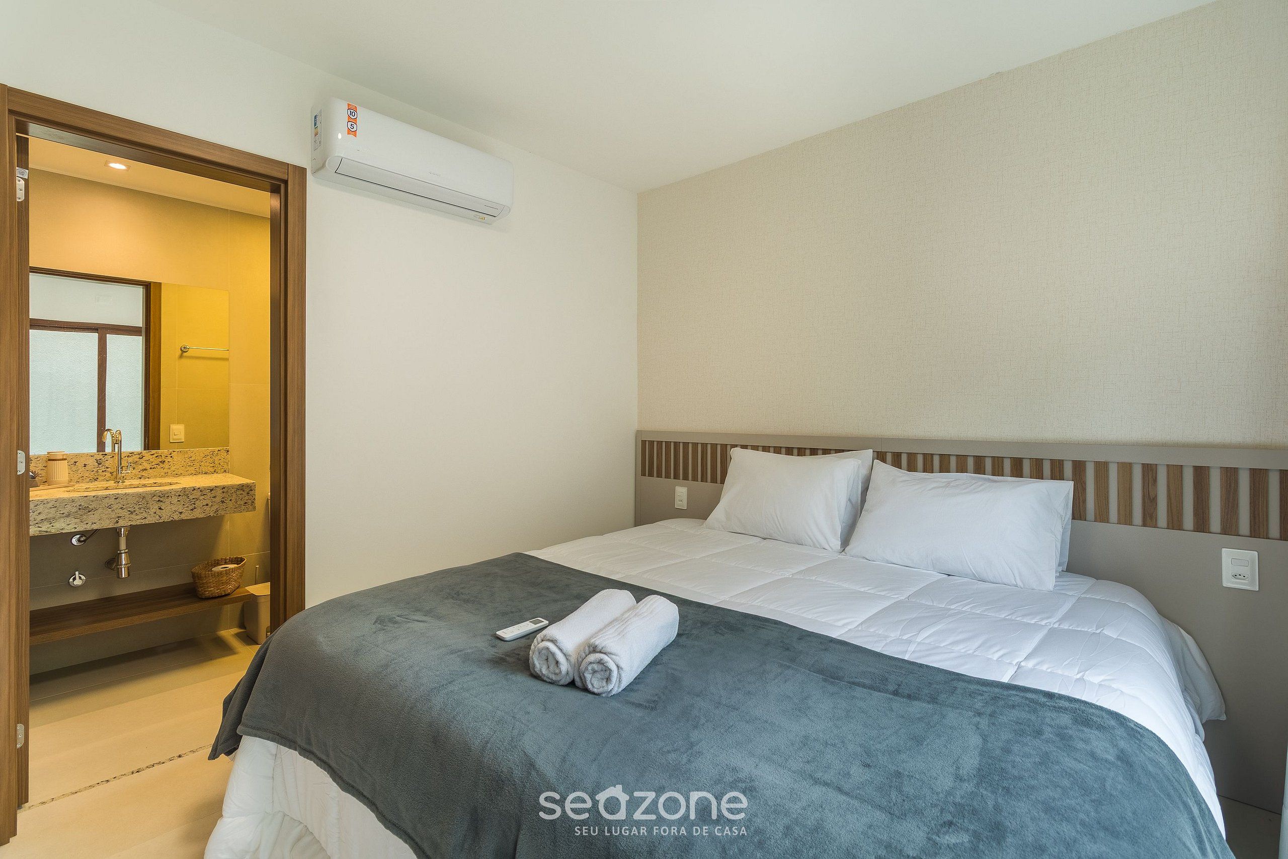 Quarto de hotel com cama, banheiro com pia e espelho, e ar condicionado.