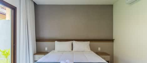 Una habitación de hotel con cama, mesita de noche, aire acondicionado de pared y ventana con cortinas.