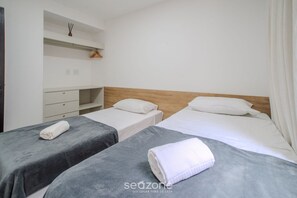 Ein Hotelzimmer mit zwei Betten, einem hölzernen Kopfteil, einer kleinen Ablagefläche mit einer Uhr und einem weißen Kleiderschrank.