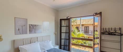 A bedroom with a bed, a ceiling fan, a window with an open door, and a view of a building outside.