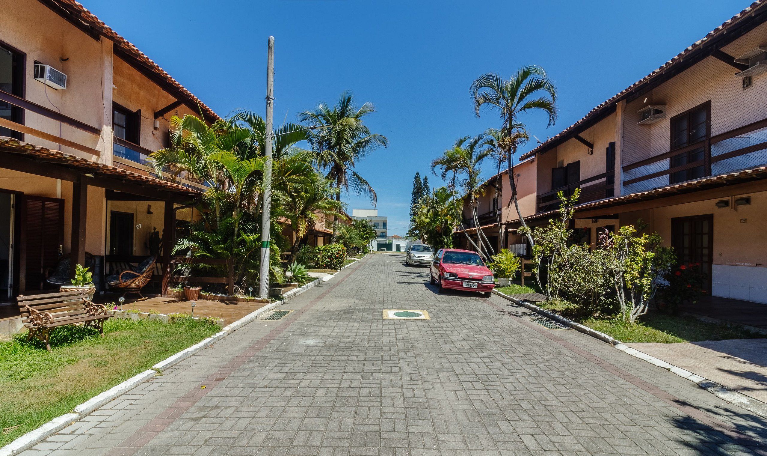 Una calle residencial con casas, palmeras y un coche rojo estacionado al lado.
