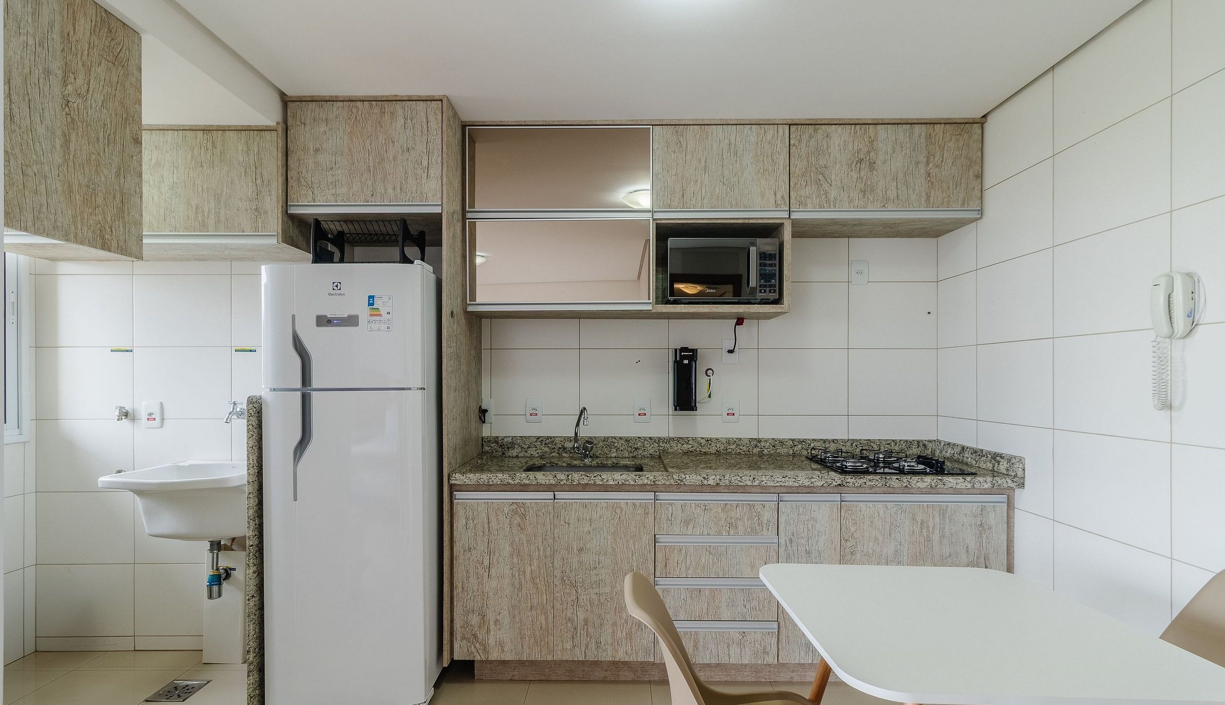 A compact kitchen with a refrigerator, microwave, sink, and a small dining table.