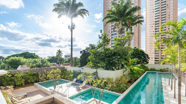 Piscina en la azotea con sillones de descanso, rodeada de vegetación y edificios altos.
