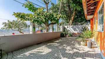A paved outdoor area with a view of the sea, surrounded by trees and potted plants.