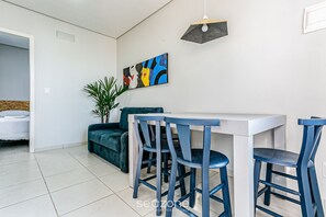 Ein moderner Essbereich mit einem weißen Tisch und blauen Stühlen, einem Bild an der Wand und einer Pflanze.