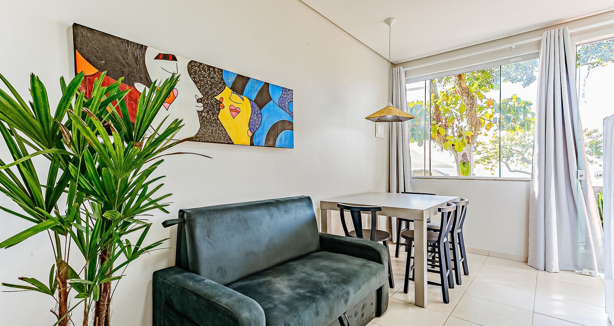 A room with a sofa, a dining table with chairs, a potted plant, and artwork on the wall.