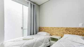 Habitación de hotel con dos camas, una ventana con cortinas y un cabecero con diseño que imita la madera.