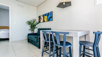 A modern dining area with a white table and blue chairs, a painting on the wall, and a plant.