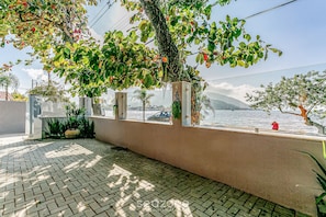 Ein gepflasterter Außenbereich mit Blick auf das Meer, eine Mauer mit einem Fenster und etwas Grün.