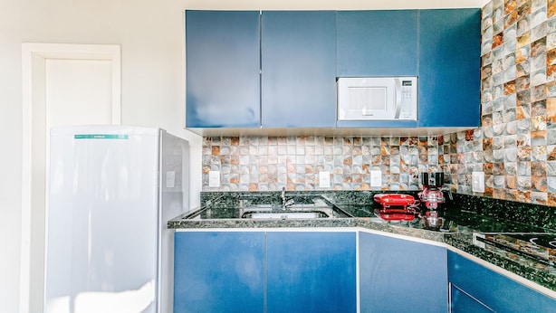 A kitchen with blue cabinets, a white refrigerator, a microwave, and a tiled backsplash. - Fit w/ Beautiful View of Lagoa da Conceicao Sdr002 (Florianópolis)