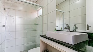 Uma casa de banho moderna com cabine de chuveiro em vidro, uma sanita branca com bancada preta e um espelho grande acima da sanita.