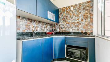 A modern kitchen with blue cabinets, a microwave, a built-in oven, and a mosaic backsplash.