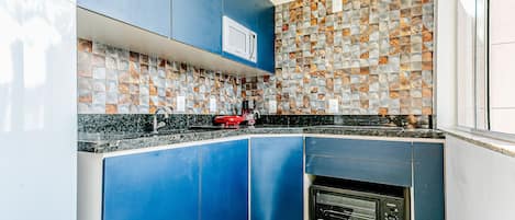 Una cocina moderna con armarios azules, un microondas, horno empotrado y salpicadero de mosaicos.
