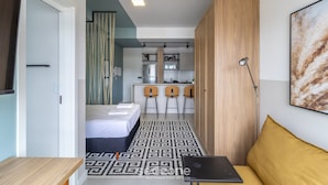 Una habitación compacta con cama, escritorio con ordenador portátil, sofá, kitchenette y baño.