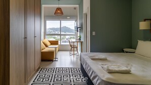 Habitación de hotel con cama, escritorio, silla y vista a un paisaje urbano a través de un ventanal grande.