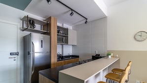 Cocina moderna con refrigerador de acero inoxidable, gabinetes de madera, encimera negra y barra con taburetes.