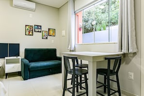 A room with a green sofa, a small white table, two black chairs, and a window with curtains. - Decorated Studio Facing the Lagoon Sdr009 (Florianópolis)