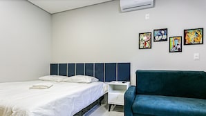 Una habitación de hotel con una cama, una mesita de noche, un sofá verde azulado y cuatro cuadros en la pared.